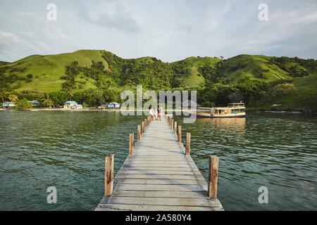 Pontile in legno nella parte anteriore del verde paesaggio collinare con capanne sulla spiaggia, Komodo, Indonesia Foto Stock