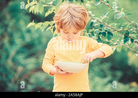 Abitudini alimentari. Kid tenere cucchiaio. Piccolo bambino di gustare pasti fatti in casa. La nutrizione per i bambini. Poco toddler boy porridge di mangiare all'aperto. Avendo grande appetito. Nutrizione organica. Nutrizione sana nozione. Foto Stock