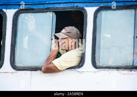 Un uomo cubano nei suoi anni 50, con un cappuccio, a cavallo dell'autobus; Camaguey, Cuba Foto Stock