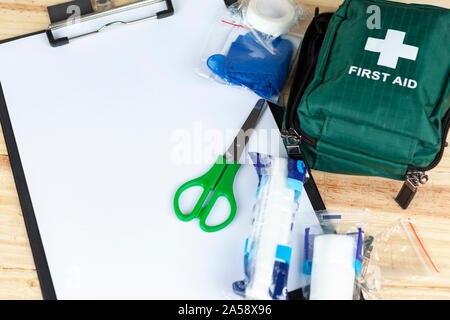 Green kit di primo soccorso su di un tavolo di legno con un blocco appunti e un paio di forbici e alcune medicazioni Foto Stock