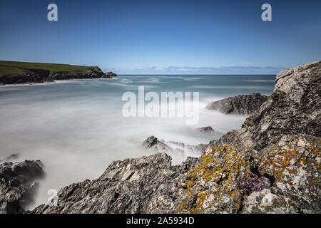 Mare ghiacciato circondato da montagne rocciose e campi verdi in Porth Joke Cove, Cornovaglia, Regno Unito Foto Stock