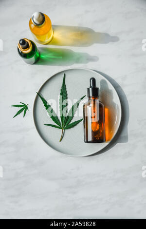 Diverse bottiglie di vetro con olio di CBD, tintura di THC e foglie di cannabis su sfondo giallo. Piatto, laici minimalismo. Cosmetici olio CBD. Foto Stock