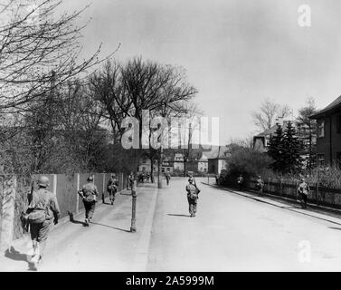 Fanti del novantesimo divisione, 3° US Army a piedi in appena catturato città di Hof, Germania Foto Stock