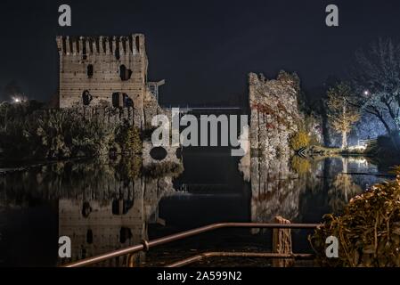 Scatto orizzontale di bellissimi castelli italiani collegati con un ponte sopra il lago di notte Foto Stock