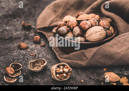 I dadi ancora vita close-up. Una piccola ciotola di colore marrone con una selezione di frutti a guscio interi - noci, nocciole, noci del Brasile e le mandorle. I dadi sono al buio su un ston Foto Stock