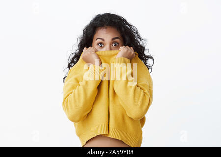 Stupiti e spaventati carino giovane americano africano studentessa nascondendo la faccia nel collare maglione, allargare gli occhi hanno teso una imboscata e si chiedeva, sollevare le sopracciglia Foto Stock