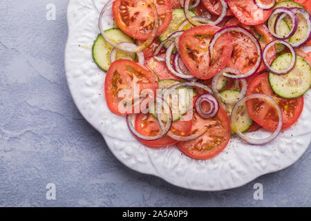 Un fresco e salutare con insalata di pomodori organico, il cetriolo e la cipolla rossa. L'insalata è visto dal di sopra. È su un blu grigio tavolo, posto in alto a destra Foto Stock