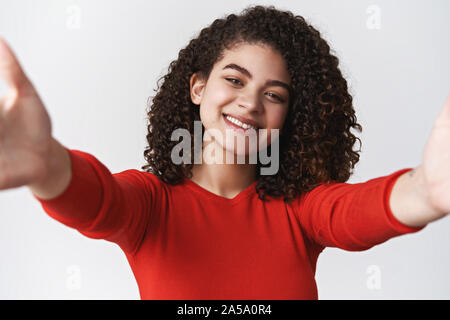 Close-up caring vivace ragazza carismatica dark curly hairstyle tendere le mani avanti tenere la fotocamera tenendo selfie sorridendo felice inviare personal Foto Stock