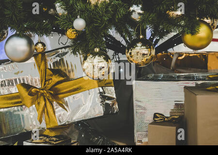 Sfondo di Natale, un sacco di scatole con doni si trova nei pressi di festosa albero di Natale, in background luci luminose. Regalo in oro lucido giacenti di confezionamento Foto Stock