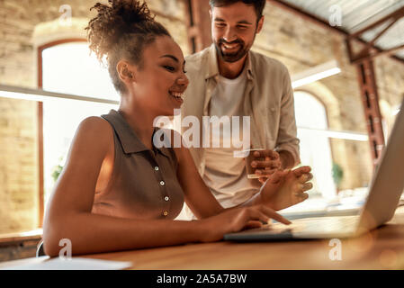 Dare consigli. Giovane e allegro uomo con tazza di caffè e di parlare con il suo collega mentre si lavora insieme in un ufficio moderno Foto Stock