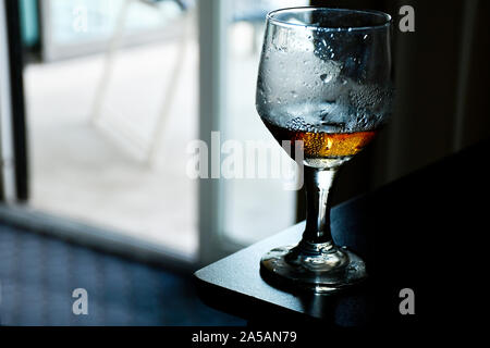 Bicchiere di whiskey con goccia di sudore sul vetro seduto su un angolo della tabella Foto Stock