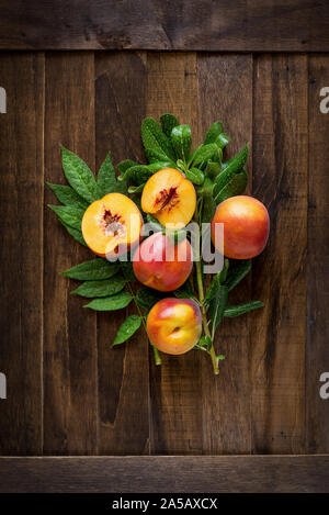 Fresco affettato pesche gialle orecchie sul tavolo di legno con foglie di colore verde Foto Stock
