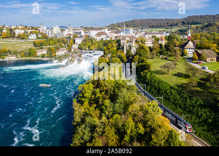 Panoramica vista aerea delle Cascate del Reno e la città di Neuhausen am Rheinfall town, Svizzera. Rosso treno svizzero e le imbarcazioni turistiche in cascata. Scogliera Foto Stock