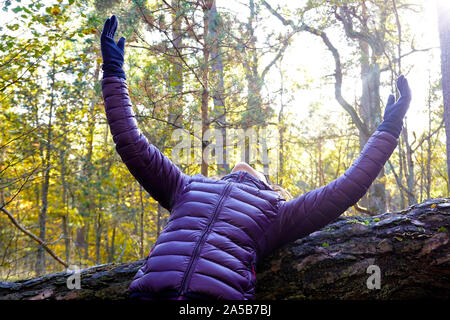 Foresta di balneazione, Shinrin yoku in giapponese. La donna si appoggia su albero caduto e fatto alzare le mani verso il sole. Natura il concetto di guarigione. Foto Stock