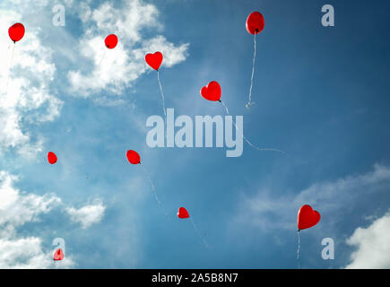 Colorate di rosso romantico cuore palloncini flottante in una soleggiata blu cielo con copia spazio concettuale del amore, romanticismo, un matrimonio o il giorno di San Valentino Foto Stock