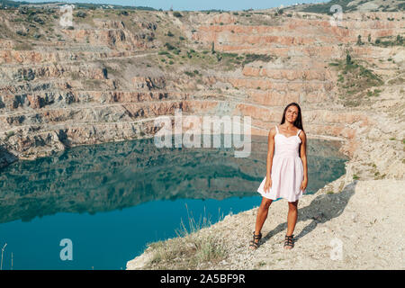 una donna con capelli lunghi si erge su una montagna accanto un lago Foto Stock