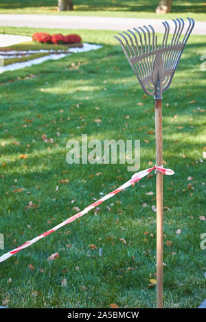 Rosso e bianco il nastro di protezione legati a una maniglia di rake separa l'area di pulizia in un parco pubblico Foto Stock