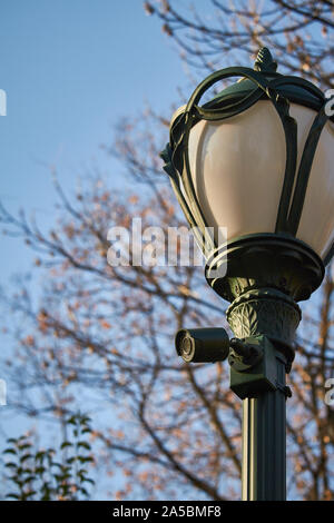 Vintage lanterna con una videocamera di sorveglianza in un parco pubblico in autunno davanti a un cielo blu, il fuoco selettivo Foto Stock