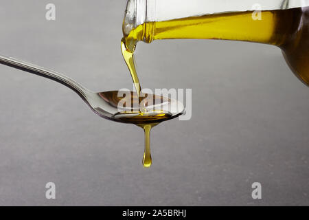 Versando l'olio d'oliva dalla bottiglia di vetro su uno sfondo grigio Foto Stock