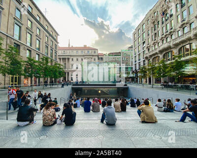 Settembre 25, 2019 L'Italia. Milano. Un sacco di persone sono seduti sui gradini vicino Apple store a Milano. Sulla scalinata, ammirando il parallelepipedo di cristallo di Foto Stock