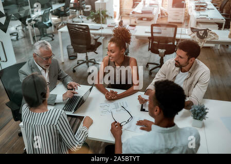 Riunione di affari. Vista dall'alto di uomo maturo in abbigliamento formale a discutere di qualcosa con il suo team multiculturale mentre è seduto al tavolo di office Foto Stock