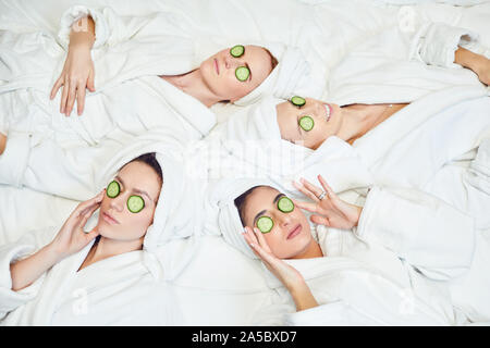 Le donne di refrigerazione in accappatoi con fettine di cetriolo sul viso Foto Stock