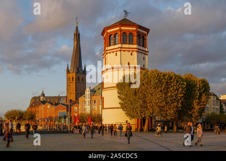 Scenario esterno di persone sulla passeggiata lungofiume del Reno a Burgplatz plaza e sullo sfondo della storica torre e chiesa nella città vecchia in sunset Foto Stock