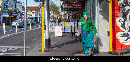 Donna islamica indossano hijab camminare durante la conversazione su un telefono mobile lungo il Victoria Street Richmond Melbourne Victoria Australia. Foto Stock