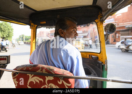 Un driver non identificato è a cavallo di un auto rickshaw attraverso le strade affollate di Jaipur. Foto Stock