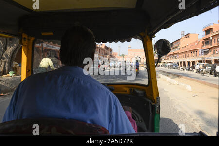 Un driver non identificato è a cavallo di un auto rickshaw attraverso le strade affollate di Jaipur. Foto Stock