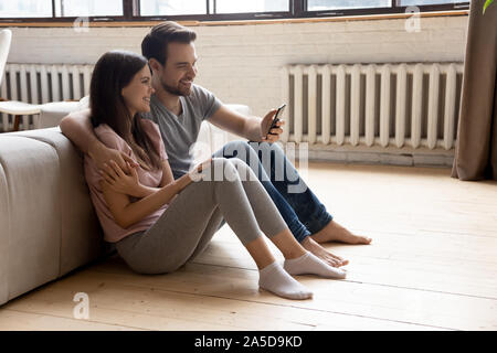 Uomo sorridente e la donna abbracciava, tramite telefono, seduto sul pavimento Foto Stock