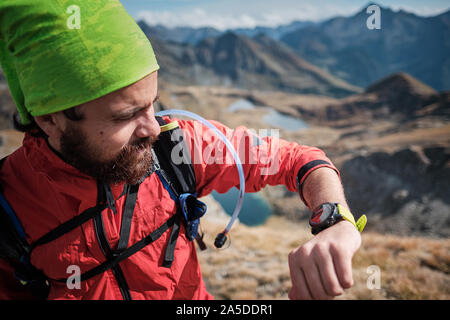 Giovane uomo guardando la traccia gps sul suo indossabile, durante le escursioni in montagna in una limpida giornata autunnale Foto Stock