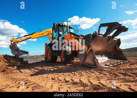 La pala caricatrice gommata escavatore con lo sfondo del campo durante lavori di movimento terra, costruzione dell'edificio Foto Stock