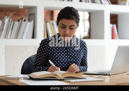Etnia indiana donna studente scrivere note la lettura di un libro di testo che studiano in ambienti interni Foto Stock