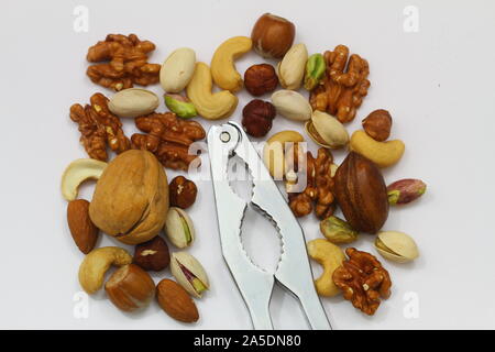 Schiaccianoci tra la selezione di pistacchi, nocciole, noci pecan, noci, anacardi e mandorle sulla superficie bianca Foto Stock