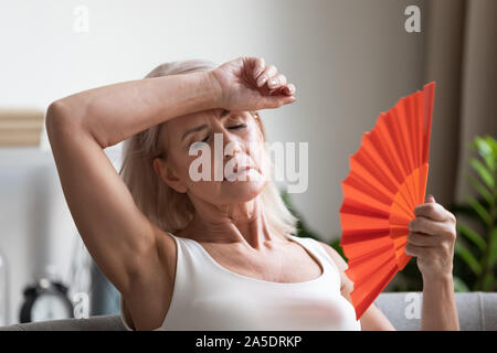 Stanco surriscaldato medio anziana signora di onda si lamentano della ventola sul calore Foto Stock