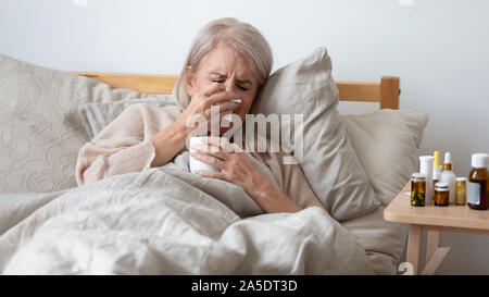 I vecchi malati donna holding fazzoletto soffia il naso nel letto Foto Stock