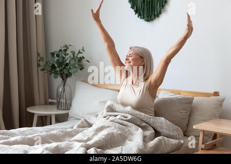 Felice donna matura stretching nel letto svegliarsi felici concept Foto Stock