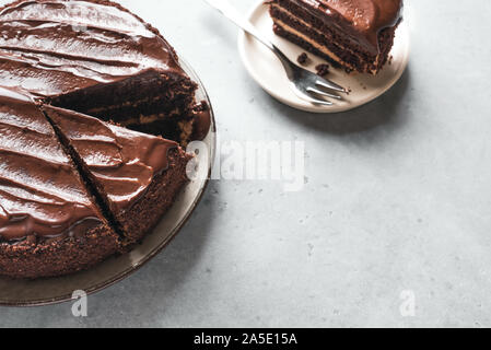 Torta al cioccolato con pezzi tagliati su sfondo grigio chiaro vicino. Classica torta al cioccolato con cioccolato fondente ganache. Foto Stock