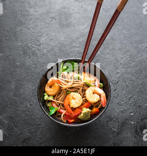 Stir fry con la sua pasta di soba, gamberi (gamberetti) e verdure. Asian cibo sano, mescolare farina fritto in un recipiente su sfondo nero. Foto Stock