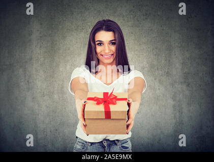 Ritratto di una bella ragazza sorridente dando una confezione regalo guardando la telecamera isolata su sfondo a parete Foto Stock