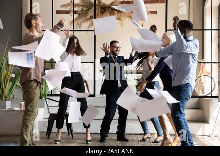 Emozionato felice multirazziale team business dancing gettando documenti di office Foto Stock