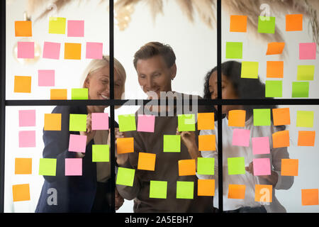 Tre felice diversi colleghi di team di scrivere le idee su foglietti adesivi Foto Stock