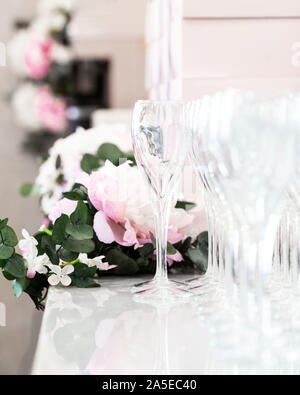 Bicchieri di champagne su tavola bianca con fiori sullo sfondo in luce naturale Foto Stock
