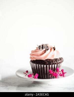 Cupcake al cioccolato con glassa rosa su sfondo bianco con fiori Foto Stock