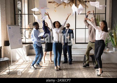 Funny happy multirazziale team aziendale la gente ballare toss paper Foto Stock