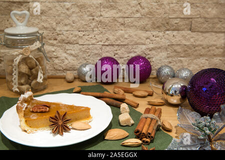 American natale torta di zucca con noci e spezie. Bellissime decorazioni di Natale, viola le palle di Natale, lo zucchero di canna e bastoncini di cannella sul mattone Foto Stock