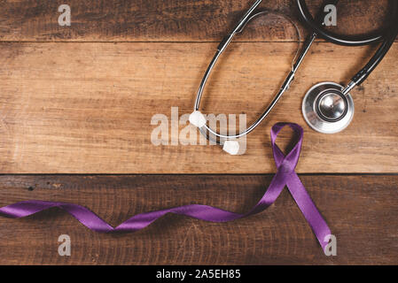 Nastro di colore viola e uno stetoscopio su un tavolo di legno. Concetto di epilessia la consapevolezza e il trattamento medico Foto Stock