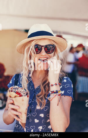 Giovane donna bionda in hat mangiare waffle bolla al festival di fragola Foto Stock