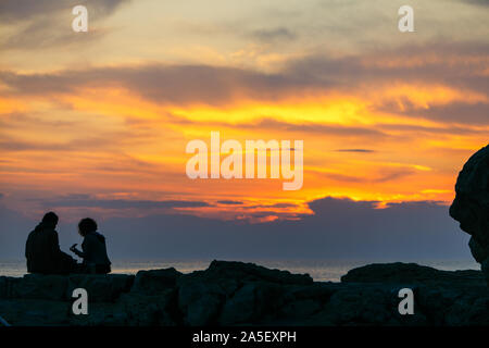 Giovane seduto sulla scogliera di roccia guardando il tramonto. Data romantico Foto Stock